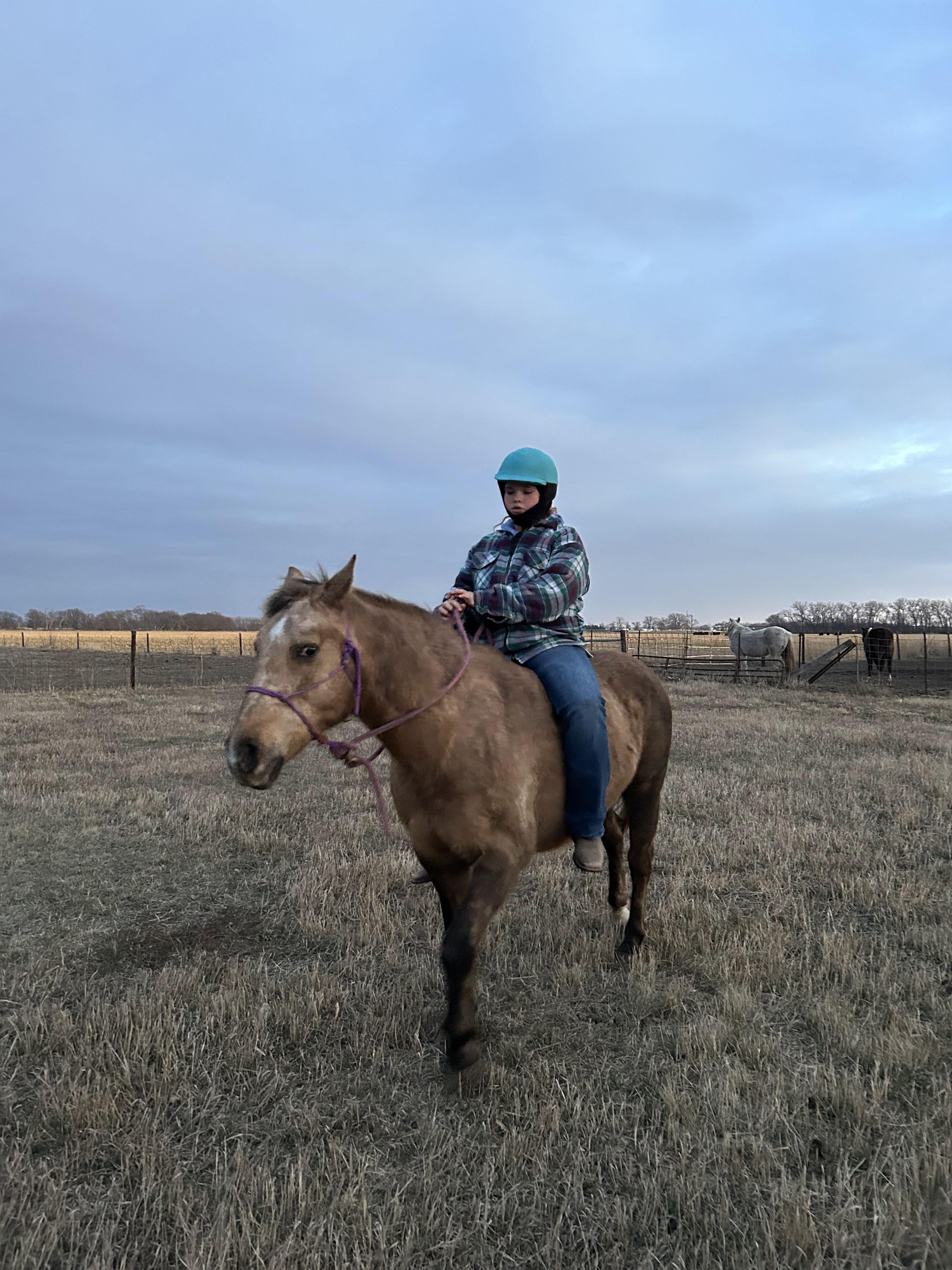 Photorealistic photo of a 13-year-old wearing a helmet riding a horse around barrels outdoors, centered rider with motion blur and dust, natural lighting, family-friendly
