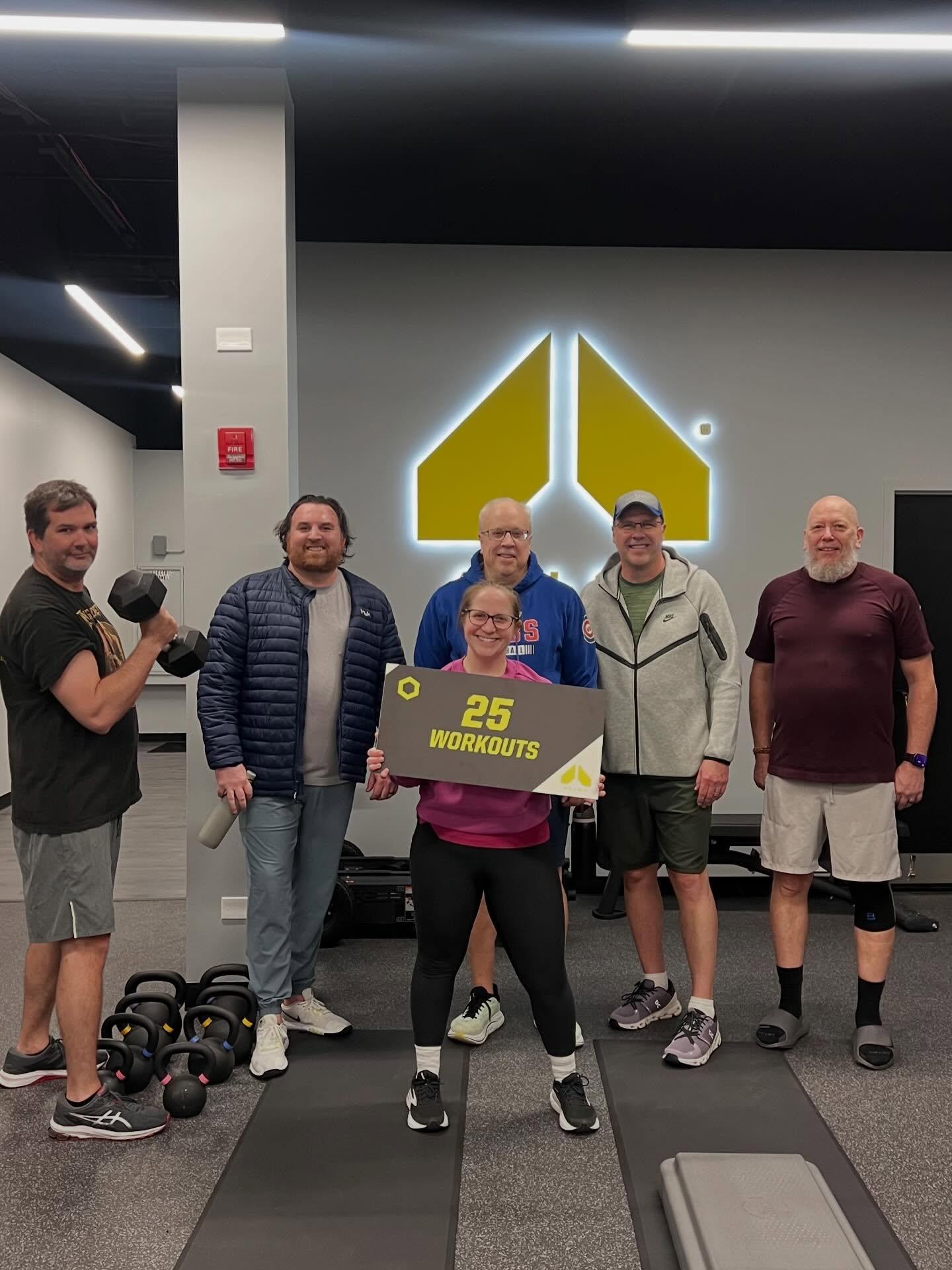 Client celebrating 25 workouts with small group personal training members at Alloy Personal Training Geneva in a functional strength training gym with kettlebells and weights in Geneva Illinois