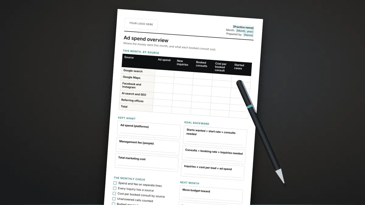 The printed ad spend tracker on a dark desk beside a pen, with spend, fee and cost per booked consult columns.