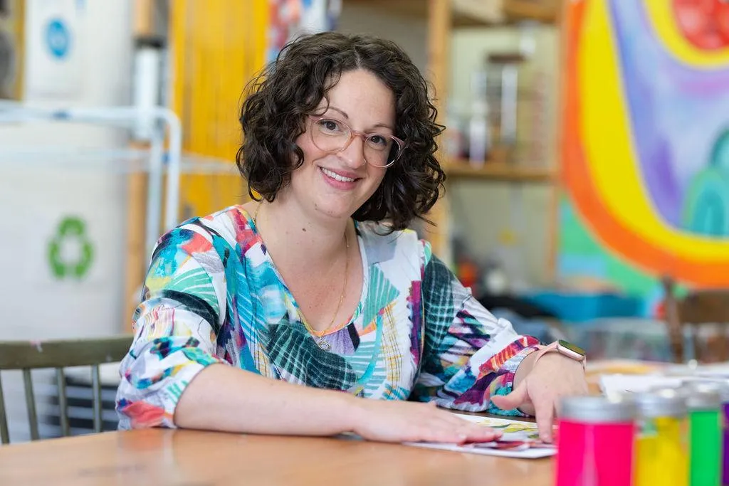 A bright lifestyle scene showing a single parent’s hands arranging colorful craft supplies on a table, natural daylight from a nearby window, candid warm mood, photorealistic editorial style, family-friendly atmosphere.