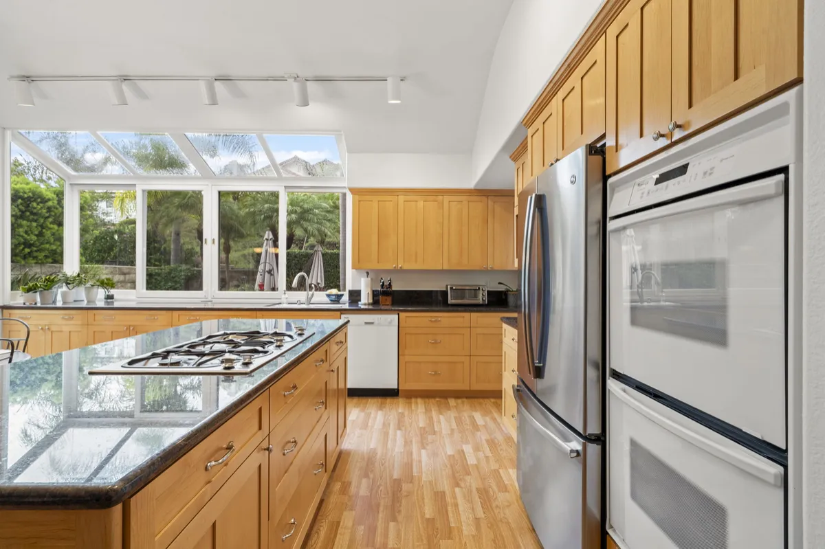 Kitchen with wood cabinets, stainless steel appliances, a gas cooktop, wood flooring, and windows above the sink.