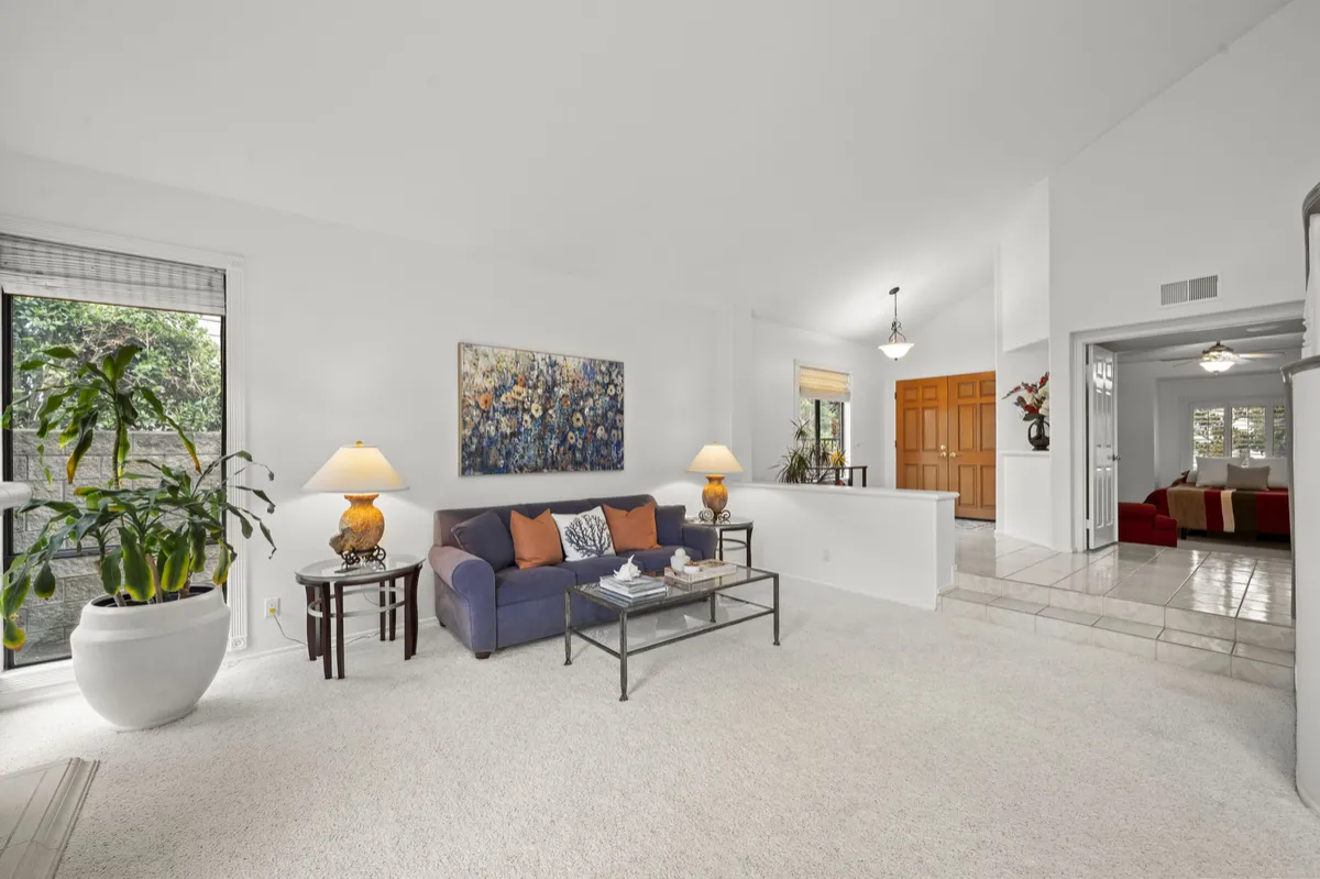 Living room with a blue sofa, glass coffee table, light carpeting, and a view toward the front door.