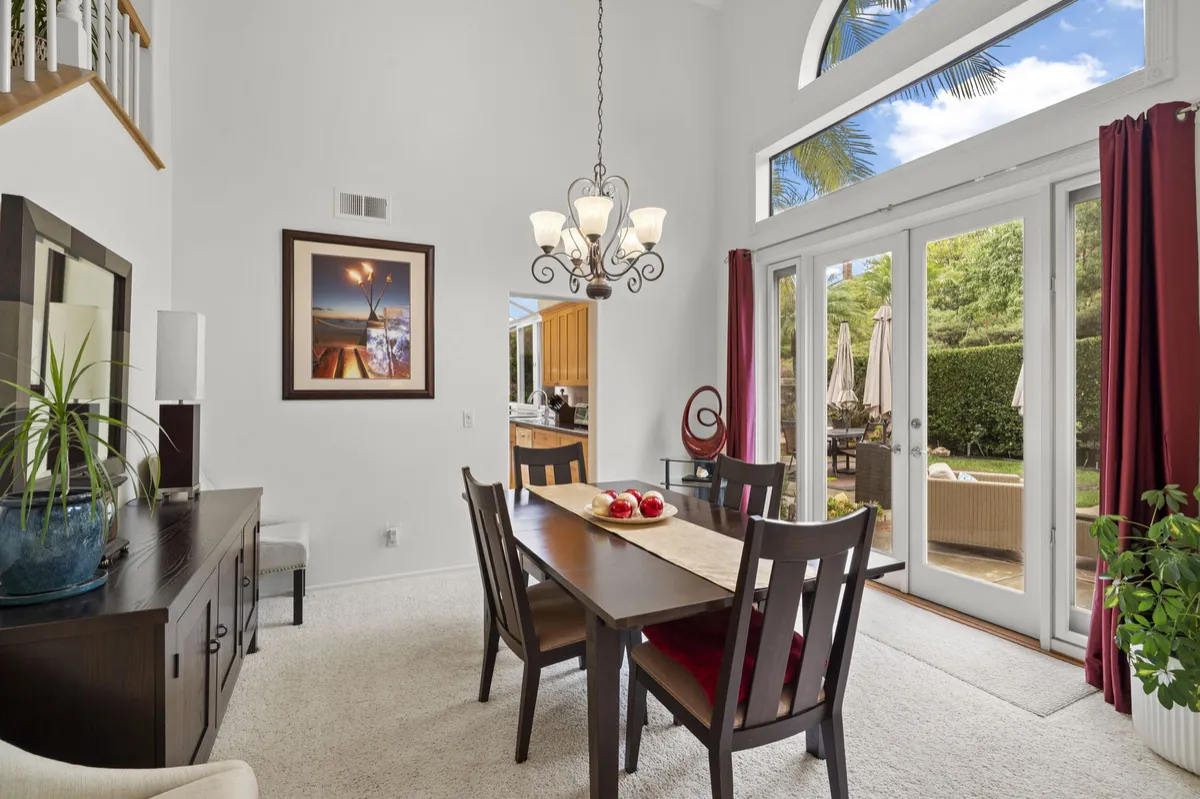  Dining area with a chandelier, dark wood table, tall windows, and glass doors facing the backyard.