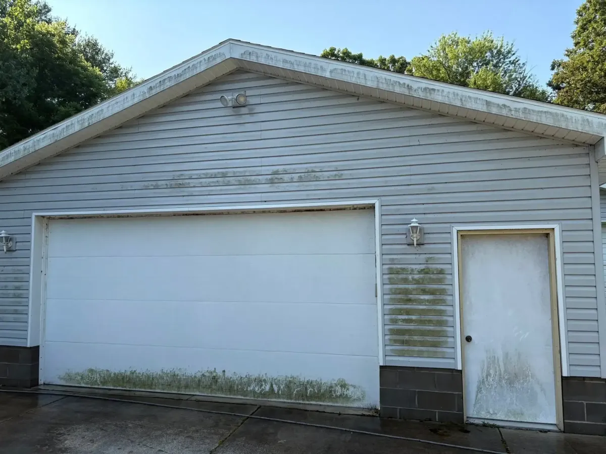 A detached garage with visible mildew and dirt near the bottom. The door next to the garage door has streaking and dust.