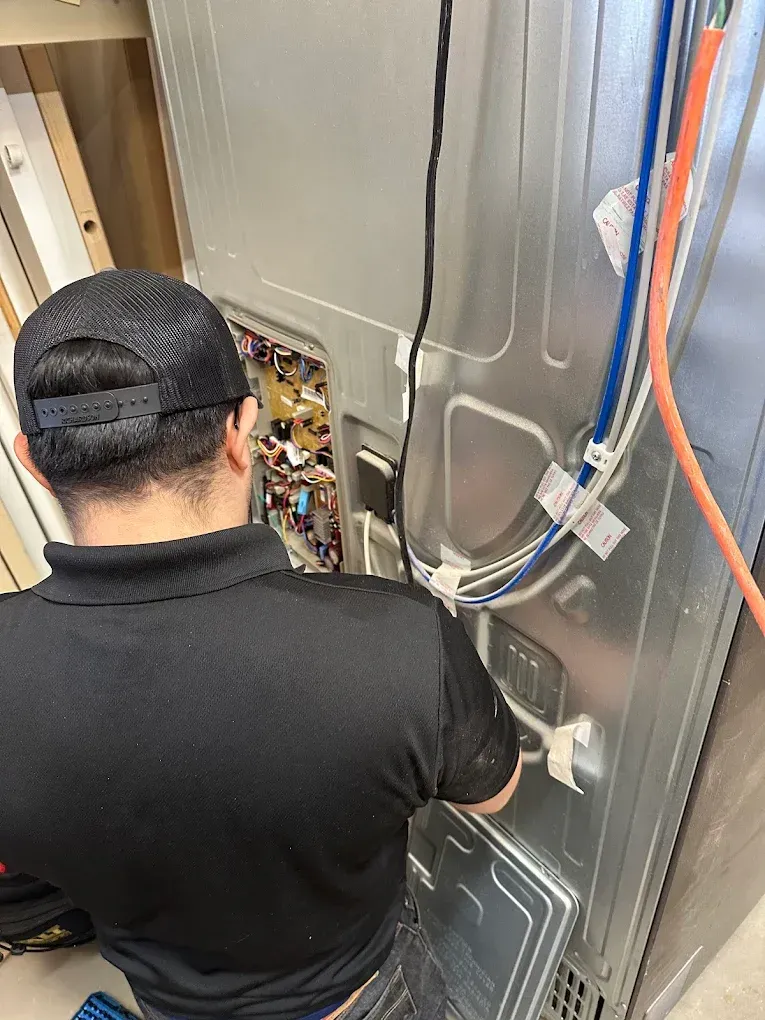An appliance repair professional using a digital multimeter to test internal electrical components inside a residential refrigerator in Modesto, CA near the North Beyer Park area.