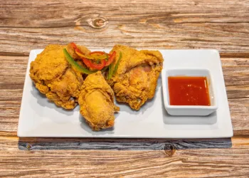 Golden Jamaican fried chicken sided with hot sauce and served on a white rectangular plate.