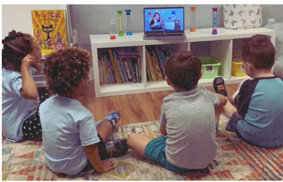 Students sit in a semicircle watching the teacher on a laptop