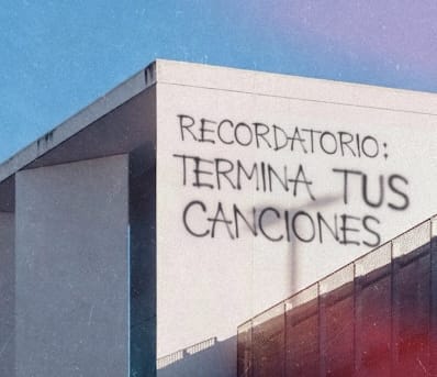 Fotografía urbana de la parte superior de un edificio minimalista bajo un cielo despejado. En la pared blanca destaca un graffiti con letras negras estilo "handstyle" que dice: "RECORDATORIO: TERMINA TUS CANCIONES". La imagen tiene un ligero grano vintage y tonos cálidos en las esquinas.