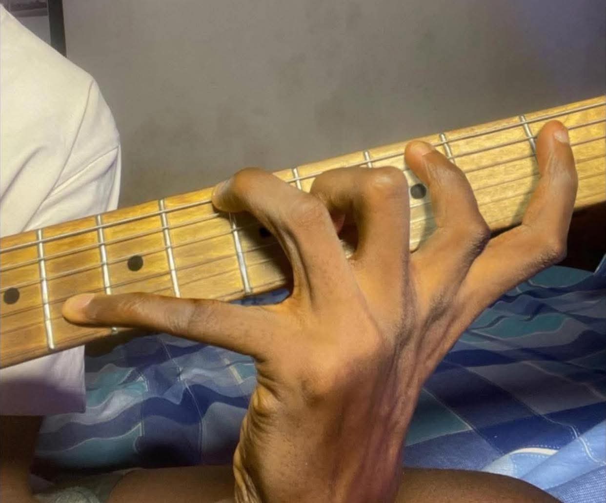 Primer plano de una mano humana extremadamente distorsionada y con dedos extra largos realizando una postura de acorde imposible en el mástil de una guitarra eléctrica, abarcando casi todo el diapasón de forma surrealista.