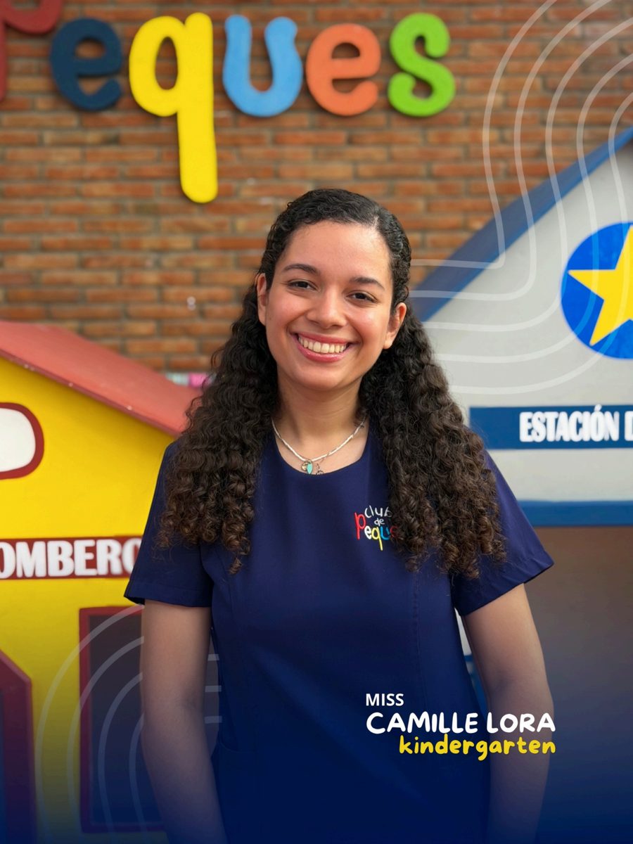 Waist-up portrait of Miss Camille Lora smiling, wearing a navy polo, in front of a colorful 'Peques' sign.