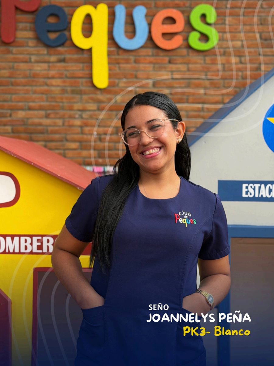 Waist-up portrait of Seño Joannelys Peña wearing glasses and a navy polo, in front of a colorful 'Peques' sign.