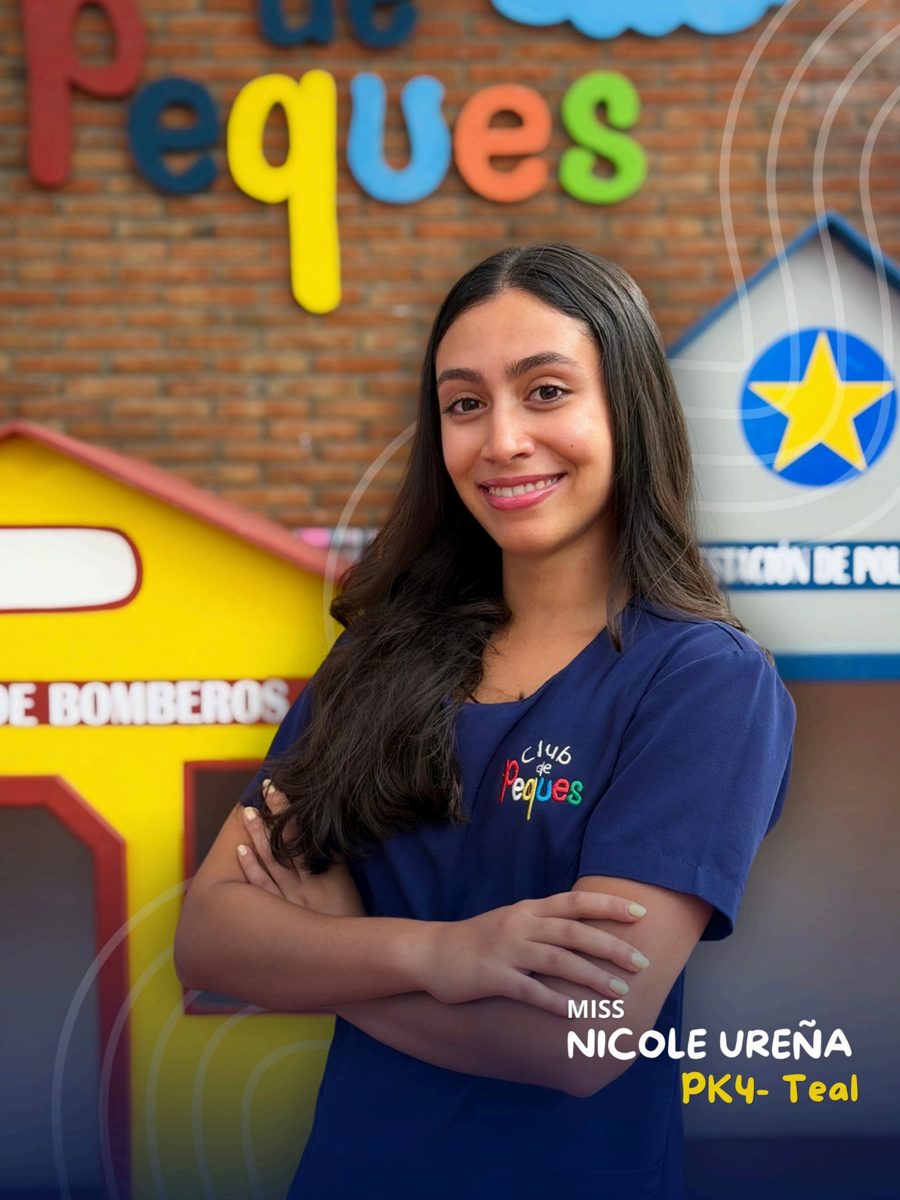 Waist-up portrait of Miss Nicole Ureña with crossed arms, wearing a navy polo, in front of a colorful 'Peques' sign.