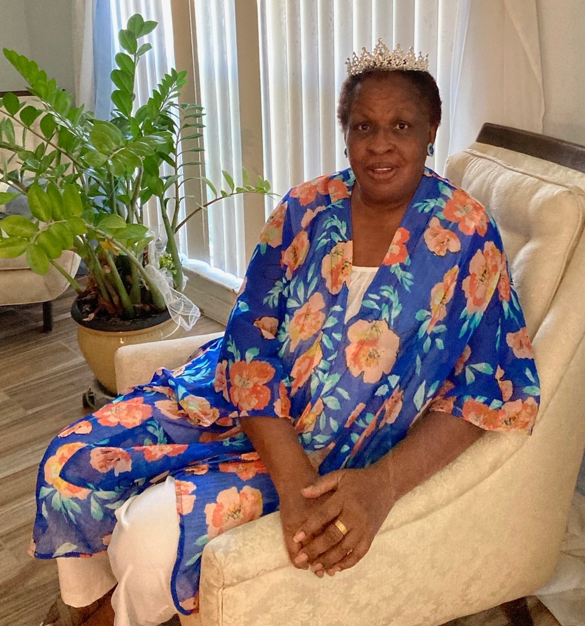 Queen Gladys seated in a floral outfit wearing her tiara