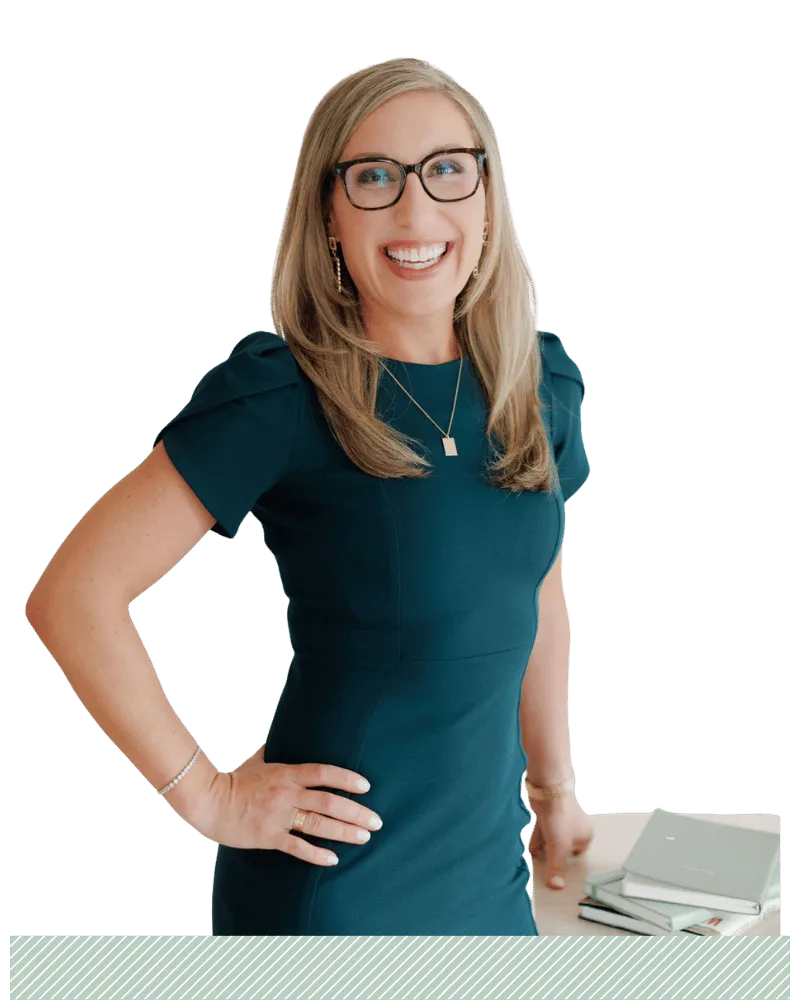 Kimberly, a blonde woman wearing think rimmed glasses and a teal dress with her hand on her hip.