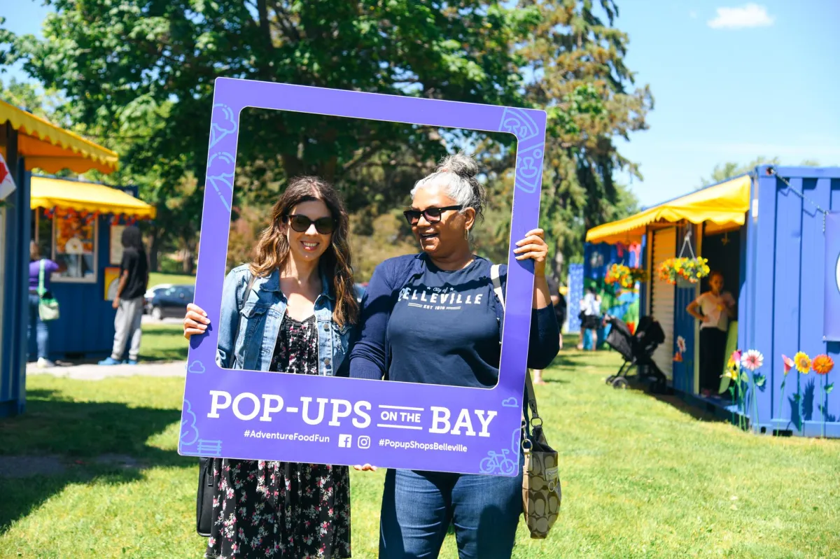 Michelle Lochan from the City of Belleville smiling alongside a guest while posing with a Pop-Ups on the Bay photo frame at West Zwick’s Park.