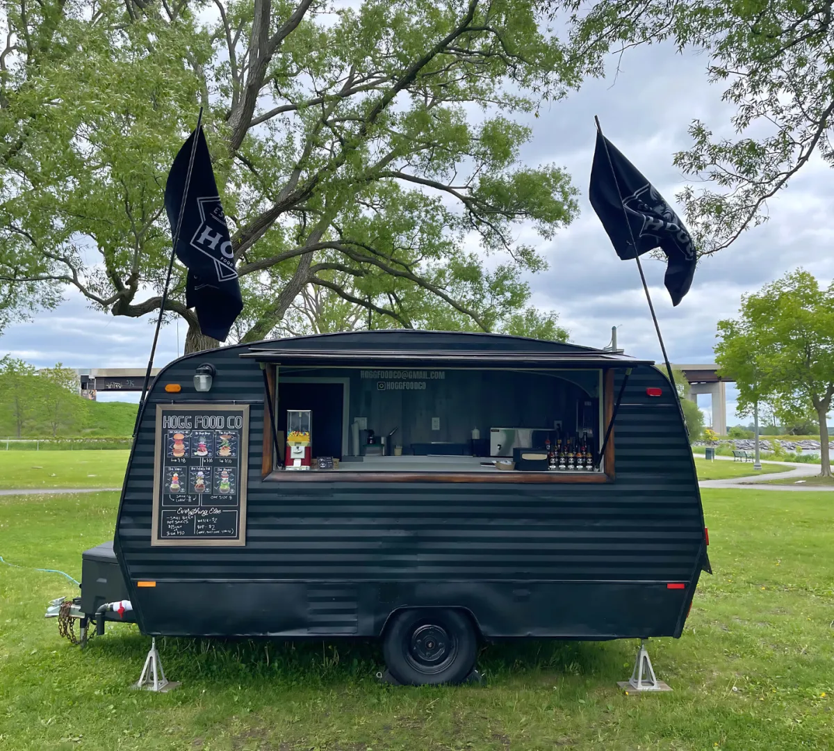 Hogg Food Co. vendor James Hogg displaying bottles of signature hot sauce and a tray of crispy fried chicken at Pop-Ups on the Bay in Belleville, ON