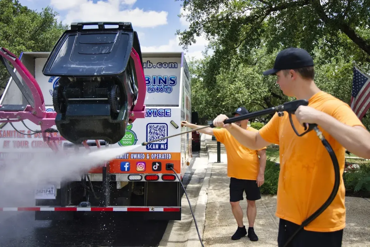 Trash bin cleaning service worker using high-pressure hot water to clean residential trash cans curbside in San Antonio.
