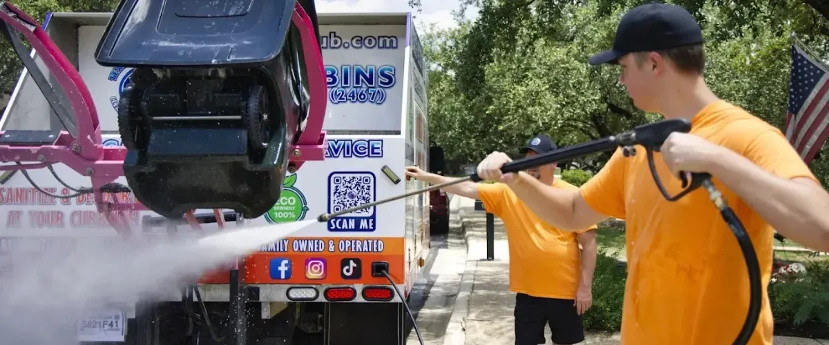 Worker using high-pressure spray to sanitize trash bin in cleaning truck system