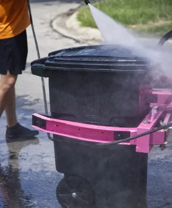 Trash can lid being cleaned with high-pressure steam and water
