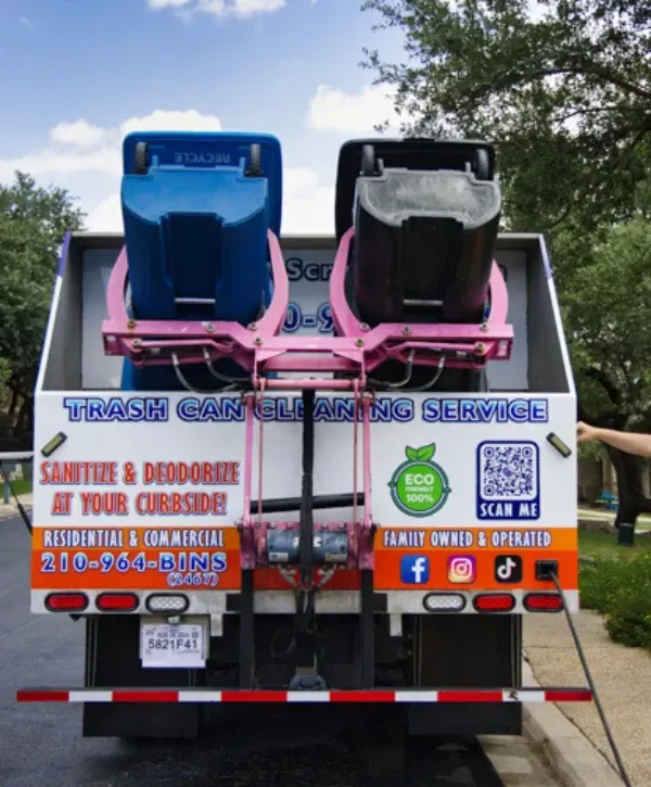 Rear view of trash can cleaning truck washing two bins at once with automated lift system