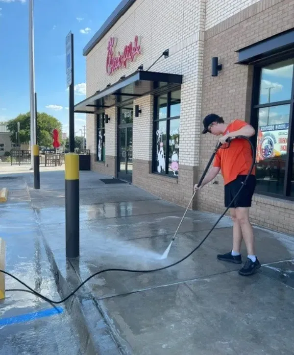 Worker pressure washing concrete sidewalk outside Chick-fil-A restaurant