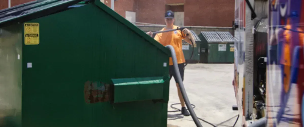 Industrial dumpster being washed with high-pressure water for sanitation.