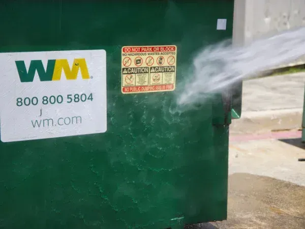 Waste Management dumpster being pressure washed and sanitized with high-pressure water spray.