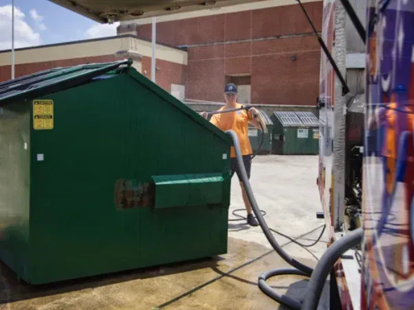 Technician cleaning a commercial dumpster using professional pressure washing equipment.