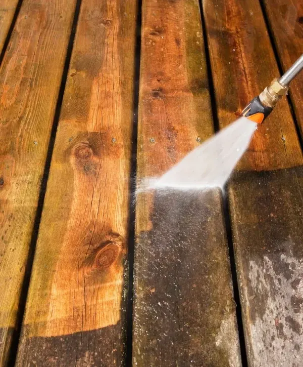 Close-up of pressure washer cleaning a wooden deck surface.