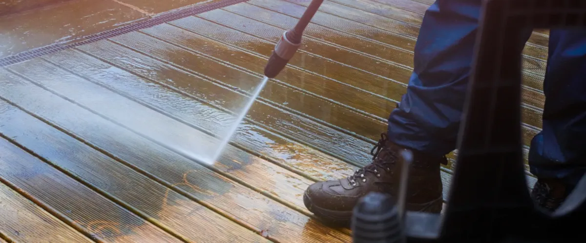 Worker pressure washing a wooden deck to remove dirt and grime.