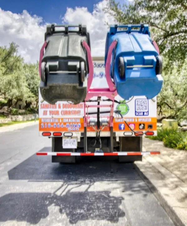 Rear view of a trash can cleaning truck lifting residential bins for curbside sanitizing service.