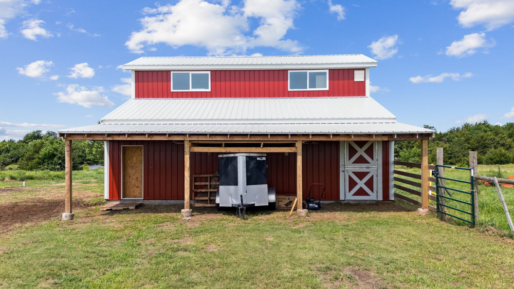 Front view of the red barn at Rock n Wood Farm & Ranch in Pawnee, Oklahoma, featuring white trim, covered livestock area, and open green pasture.
