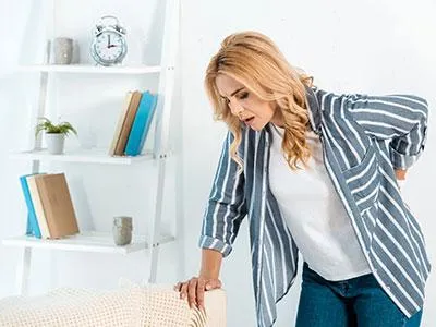 Woman experiencing back pain, holding her lower back, symbolizing relief through specialized head, neck, and back pain treatments at Naturopathic Physicians Group.