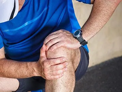 Man holding knee in discomfort, representing Naturopathic Physicians Group's holistic treatment for knee pain, hip arthritis, and foot pain in Scottsdale.