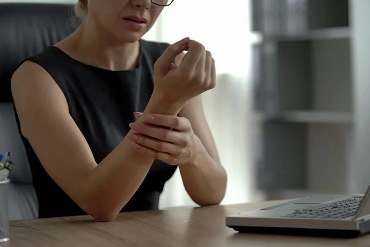 Woman dealing with wrist pain while working, representing wrist and hand treatments for pain relief and improved mobility.