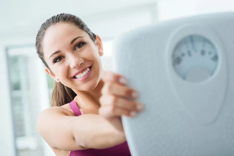 Smiling woman holding a scale, symbolizing successful weight management with personalized naturopathic care at Naturopathic Physicians Group.