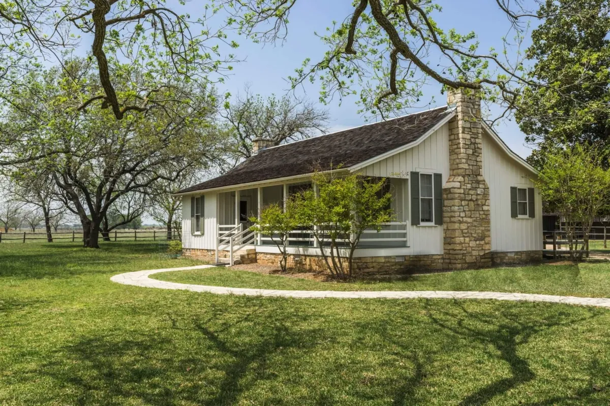 Wide-angle exterior of a modern Texas ranch-style home remodel by Evoren Development at sunset, featuring native limestone siding, expansive black-frame windows, and luxury xeriscape landscaping.