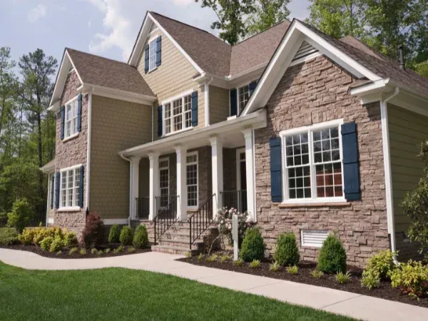 A luxurious Southern-style house with stone and siding facade, blue shutters, and manicured landscaping under a blue sky.