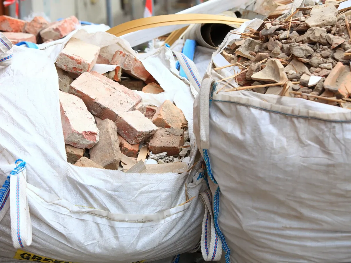 Two large white woven bags filled with construction debris, including bricks and broken concrete pieces.
