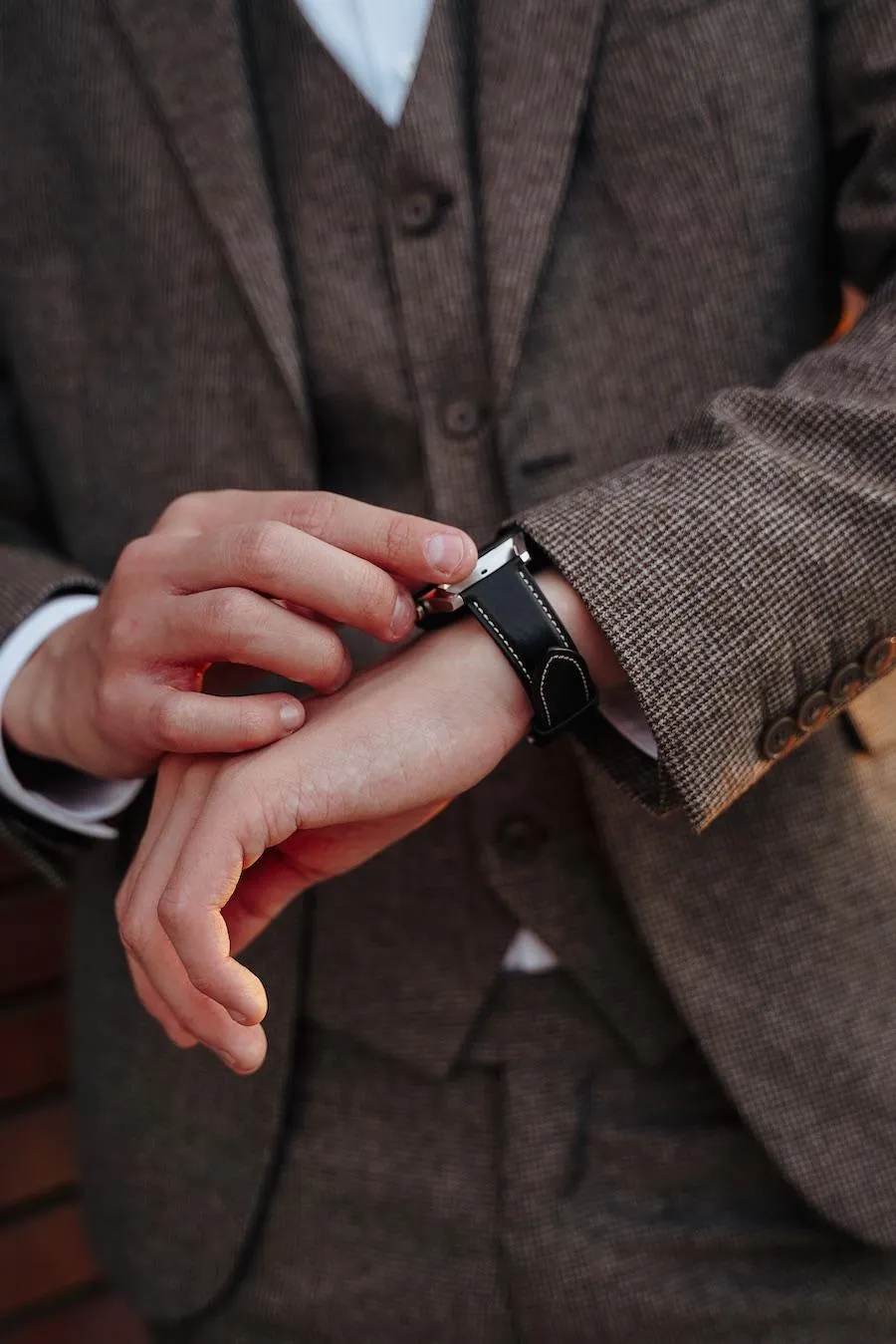 Man checking his watch wearing a brown suite