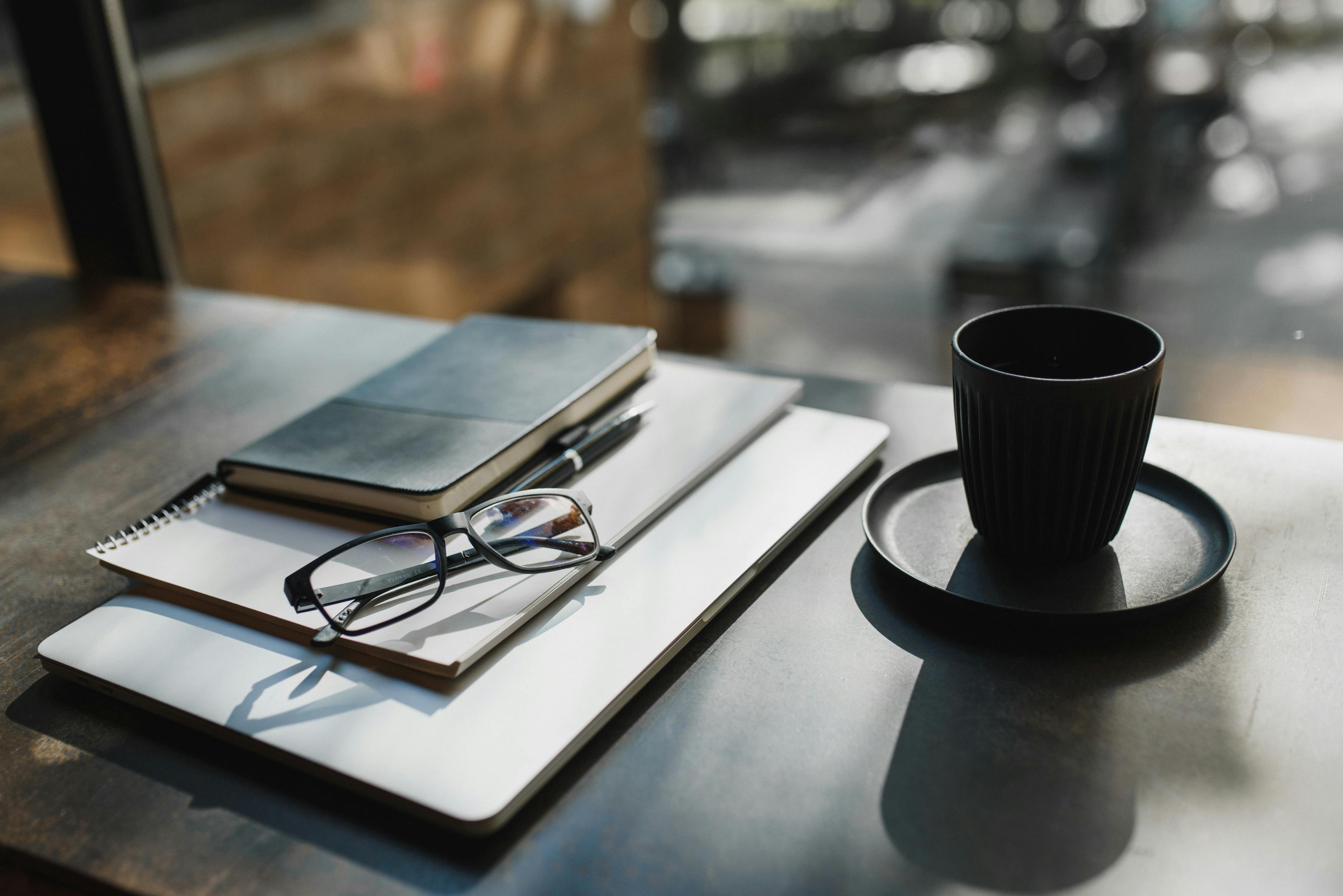 A professional journal and a warm drink on a desk, with a blurred dental practice in the background, symbolising intentional leadership and recovery.