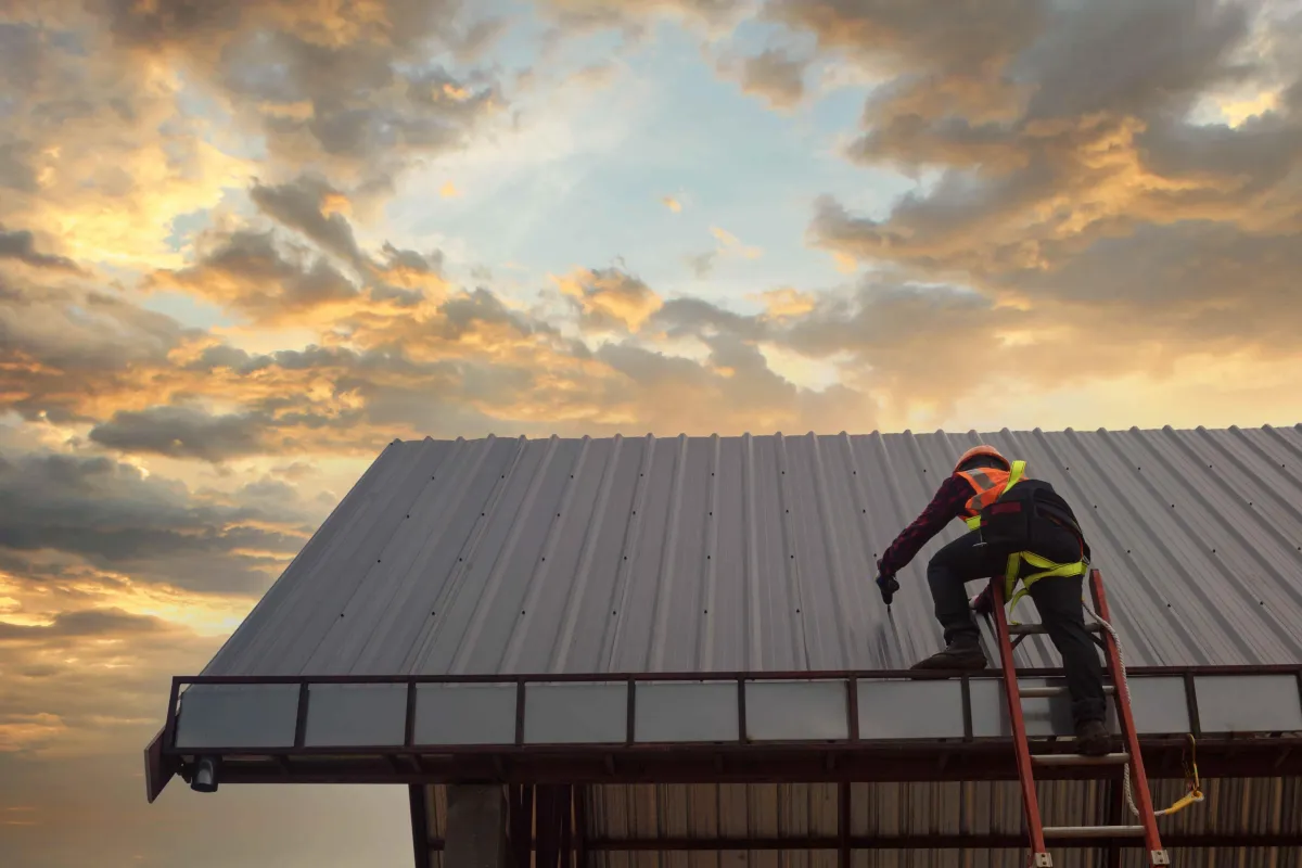 Roofer climbing ladder onto a metal roof with clouds in the background in Windsor Ontario