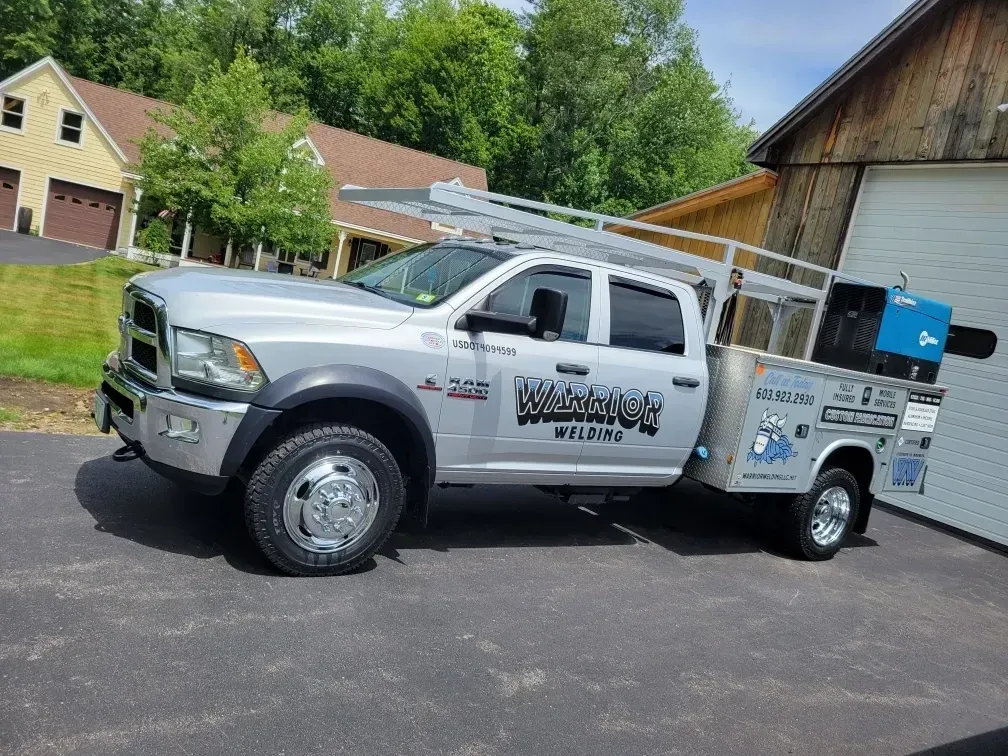 Warrior Welding branded truck and trailer setup in forested autumn location, representing fully mobile welding fleet in New England