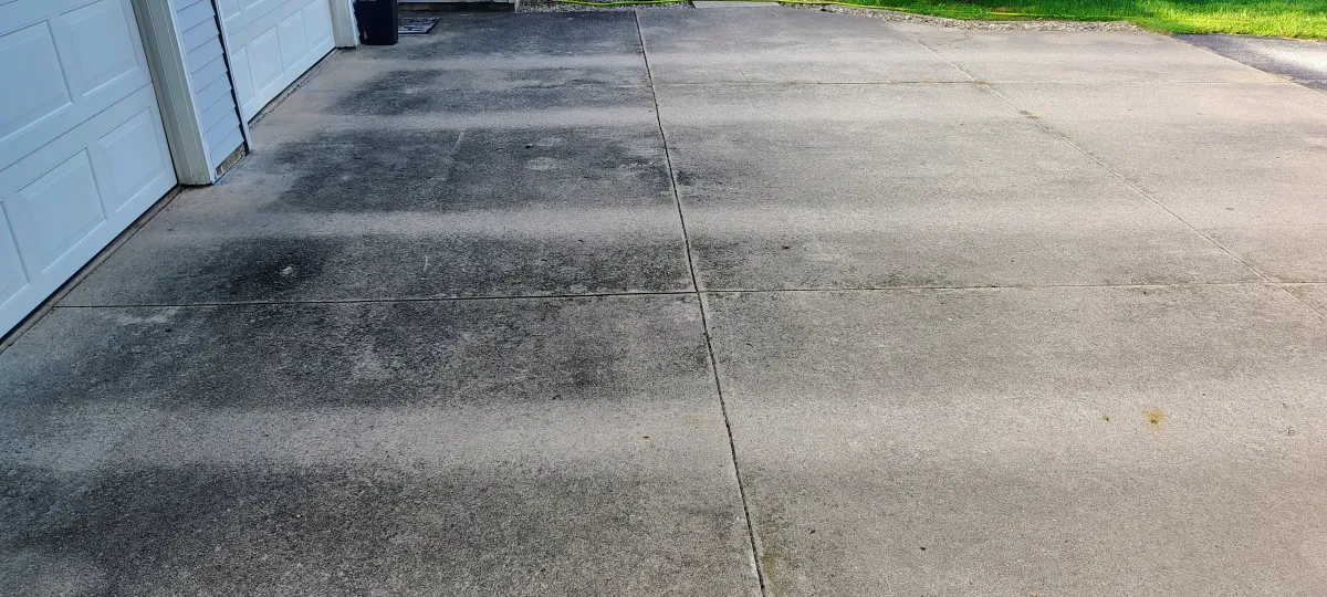 Dirty concrete driveway and walkway covered in dark surface stains before pressure washing.