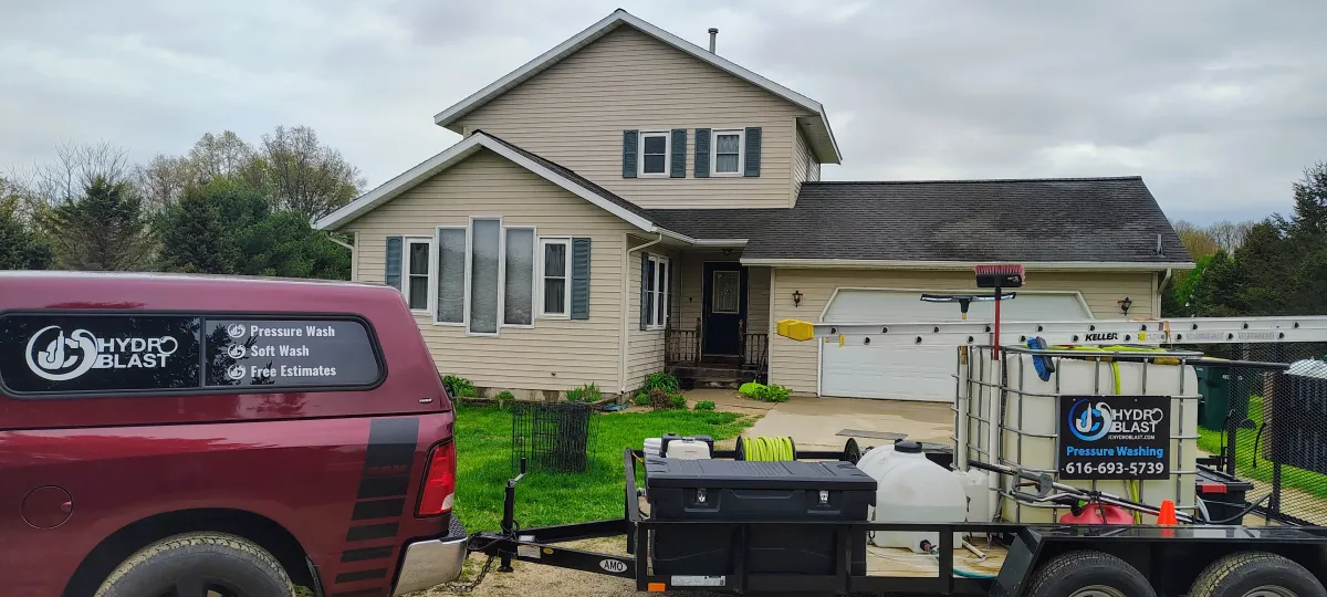 JC Hydro Blast truck and pressure washing equipment trailer parked outside a two-story West Michigan home.