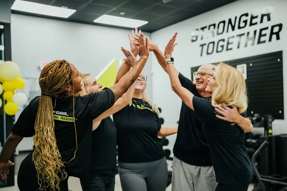 Group high-five in gym under "Stronger Together" sign