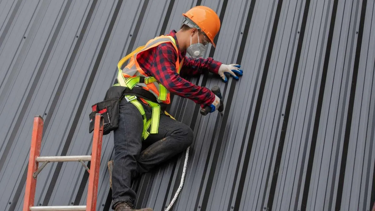 Roofer in safety gear working on metal roofing, demonstrating Hook Roofing & Construction's expertise in roof installation and repair.