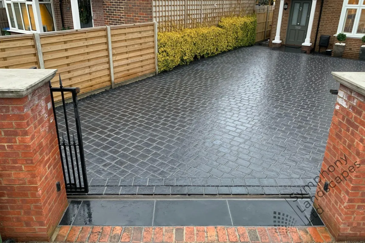 The driveway features an elegant design with interlocking pavers, providing a smooth and durable surface for vehicles. Lush greenery and colorful flowers border the driveway, enhancing its aesthetic appeal and blending harmoniously with the surrounding natural environment.