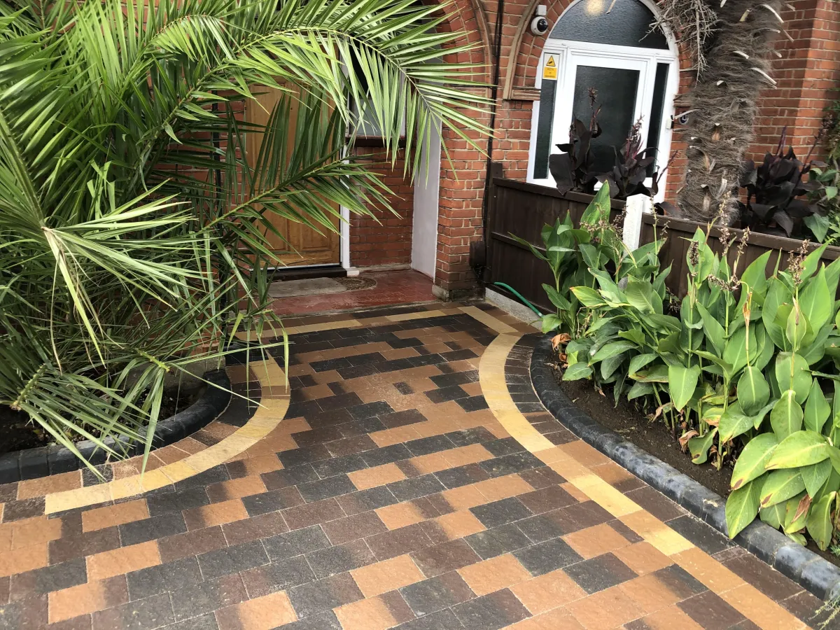 The driveway features an elegant design with interlocking pavers, providing a smooth and durable surface for vehicles. Lush greenery and colorful flowers border the driveway, enhancing its aesthetic appeal and blending harmoniously with the surrounding natural environment.