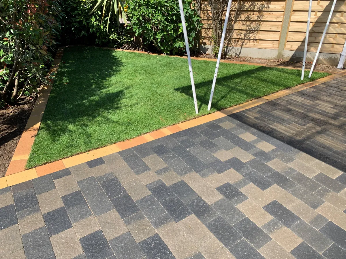 The driveway features an elegant design with interlocking pavers, providing a smooth and durable surface for vehicles. Lush greenery and colorful flowers border the driveway, enhancing its aesthetic appeal and blending harmoniously with the surrounding natural environment.